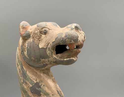 fig 8. A painted earthenware figure of a tiger-like mythical beast from the Han Dynasty featuring an arched neck, raised tail, and red and green painted stripes.