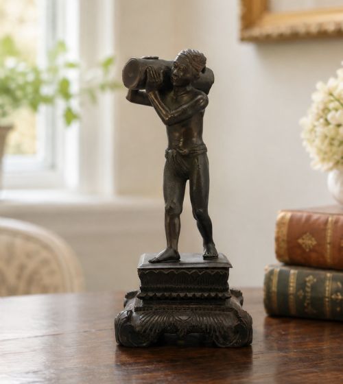 fig 1. A dark patinated bronze figurine of a man carrying a log on his shoulder, mounted on an intricately carved wooden stand.