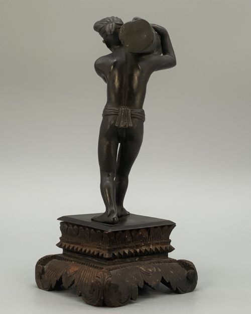 fig 9. A dark patinated bronze figurine of a man carrying a log on his shoulder, mounted on an intricately carved wooden stand.