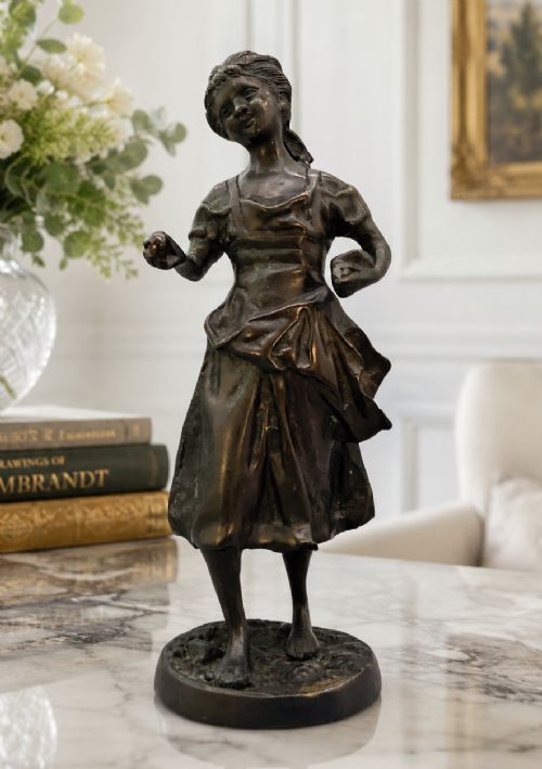 fig 1. An antique dark bronze sculpture of a young maiden wearing a draped apron dress, standing barefoot on a rounded integral base.