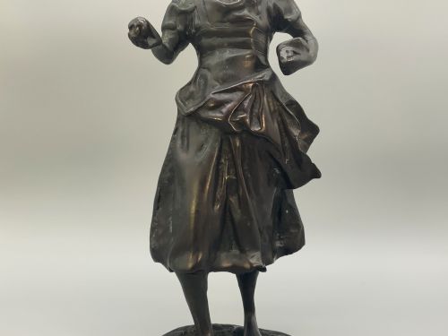 fig 4. An antique dark bronze sculpture of a young maiden wearing a draped apron dress, standing barefoot on a rounded integral base.