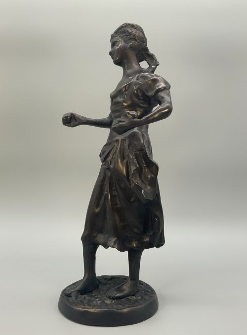 fig 6. An antique dark bronze sculpture of a young maiden wearing a draped apron dress, standing barefoot on a rounded integral base.