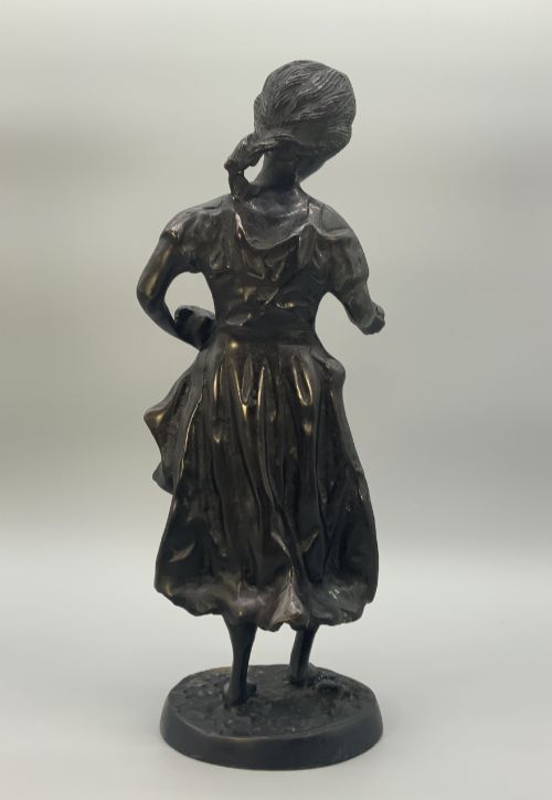 fig 7. An antique dark bronze sculpture of a young maiden wearing a draped apron dress, standing barefoot on a rounded integral base.