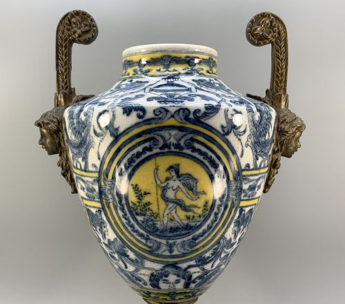 fig 3. A Renaissance Revival faience vase featuring blue and yellow glazed classical medallion artwork mounted on a cast bronze footed base with mask handles.