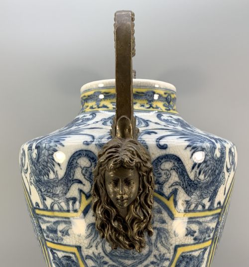 fig 7. A Renaissance Revival faience vase featuring blue and yellow glazed classical medallion artwork mounted on a cast bronze footed base with mask handles.