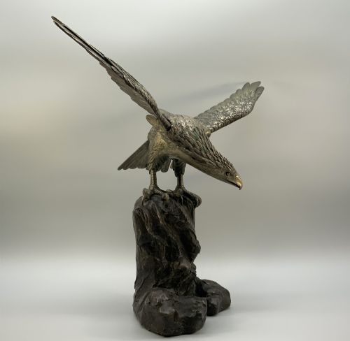 fig 3. A dark bronze sculpture depicting an eagle with outstretched wings perched on a rocky base.