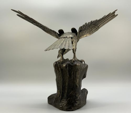 fig 5. A dark bronze sculpture depicting an eagle with outstretched wings perched on a rocky base.