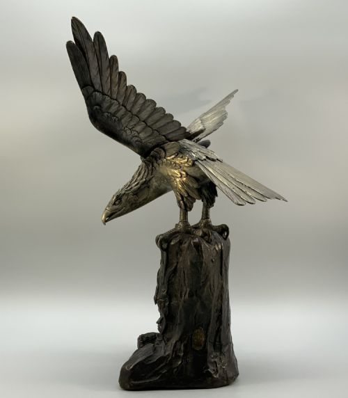 fig 6. A dark bronze sculpture depicting an eagle with outstretched wings perched on a rocky base.