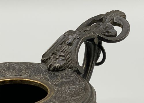 fig 8. A patinated dark bronze classical oil lamp featuring a seated putto figure on top and a scroll handle resting on a pedestal base.