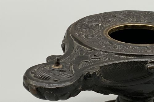 fig 9. A patinated dark bronze classical oil lamp featuring a seated putto figure on top and a scroll handle resting on a pedestal base.