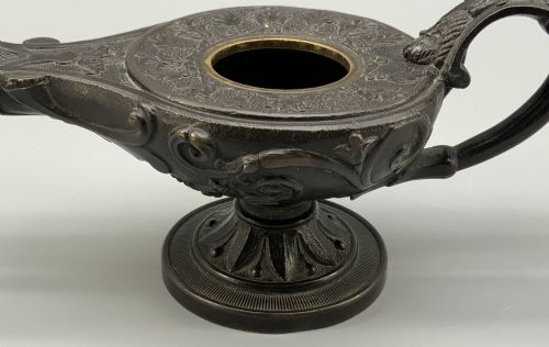fig 10. A patinated dark bronze classical oil lamp featuring a seated putto figure on top and a scroll handle resting on a pedestal base.