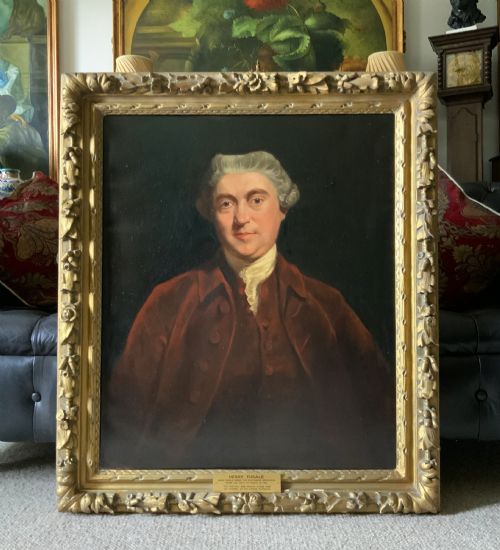 fig 1. An antique oil painting depicting a half-length portrait of a gentleman in a dark red coat, set within a carved gilded frame with a metal title plaque at the bottom.