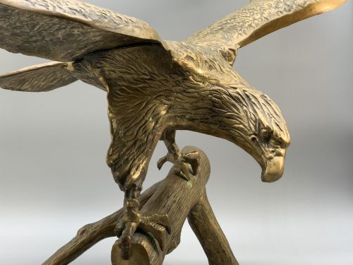 fig 3. A cast brass sculpture depicting an eagle with outstretched wings perched atop a detailed log branch.