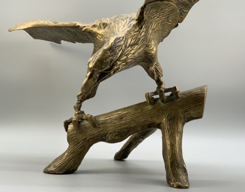 fig 9. A cast brass sculpture depicting an eagle with outstretched wings perched atop a detailed log branch.