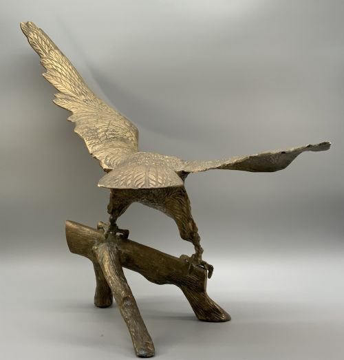 fig 10. A cast brass sculpture depicting an eagle with outstretched wings perched atop a detailed log branch.
