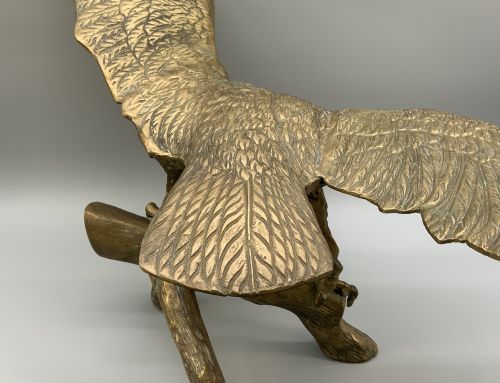 fig 11. A cast brass sculpture depicting an eagle with outstretched wings perched atop a detailed log branch.