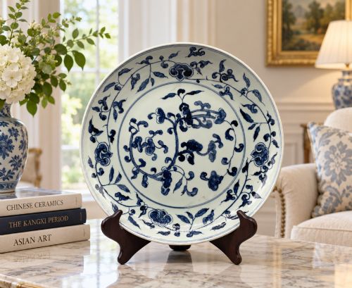 fig 1. A circular Chinese blue and white porcelain charger decorated with hand-painted scrolling foliage and floral motifs, resting on a dark wooden stand.