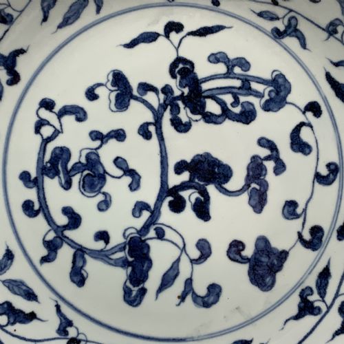 fig 4. A circular Chinese blue and white porcelain charger decorated with hand-painted scrolling foliage and floral motifs, resting on a dark wooden stand.