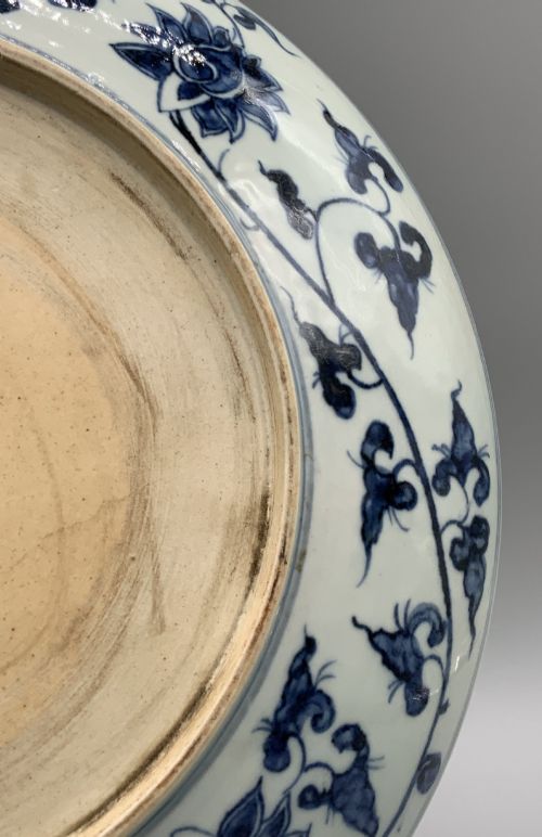 fig 12. A circular Chinese blue and white porcelain charger decorated with hand-painted scrolling foliage and floral motifs, resting on a dark wooden stand.