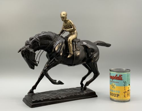 fig 2. A patinated bronze sculpture depicting a racehorse and jockey mid-stride set upon a textured rectangular bronze base.