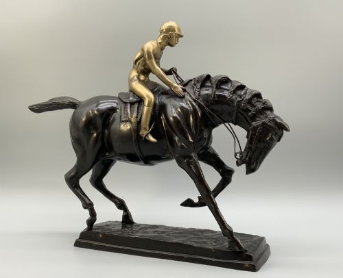 fig 6. A patinated bronze sculpture depicting a racehorse and jockey mid-stride set upon a textured rectangular bronze base.