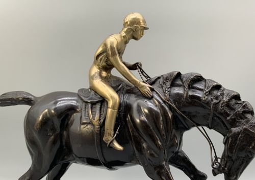 fig 7. A patinated bronze sculpture depicting a racehorse and jockey mid-stride set upon a textured rectangular bronze base.