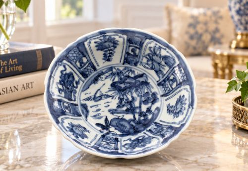 fig 1. A circular porcelain bowl with a lobed edge, decorated in cobalt blue underglaze featuring a central landscape surrounded by panelled floral reserves.
