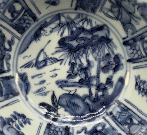 fig 3. A circular porcelain bowl with a lobed edge, decorated in cobalt blue underglaze featuring a central landscape surrounded by panelled floral reserves.