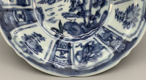 fig 5. A circular porcelain bowl with a lobed edge, decorated in cobalt blue underglaze featuring a central landscape surrounded by panelled floral reserves.