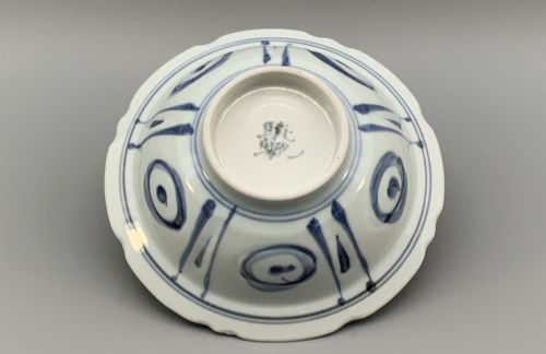 fig 9. A circular porcelain bowl with a lobed edge, decorated in cobalt blue underglaze featuring a central landscape surrounded by panelled floral reserves.