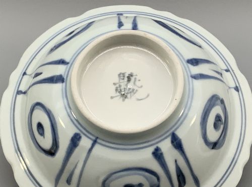 fig 10. A circular porcelain bowl with a lobed edge, decorated in cobalt blue underglaze featuring a central landscape surrounded by panelled floral reserves.