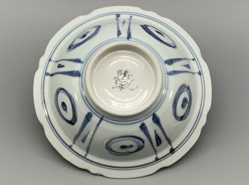 fig 11. A circular porcelain bowl with a lobed edge, decorated in cobalt blue underglaze featuring a central landscape surrounded by panelled floral reserves.