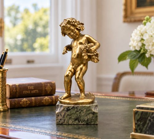 fig 1. A small gilt bronze sculpture depicting an infant Bacchus holding a bunch of grapes, set upon a square green marble plinth.