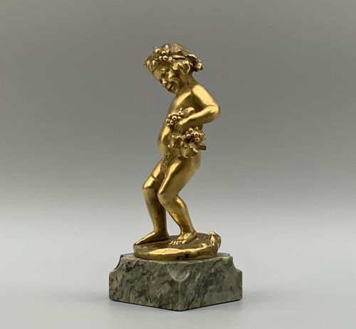 fig 3. A small gilt bronze sculpture depicting an infant Bacchus holding a bunch of grapes, set upon a square green marble plinth.