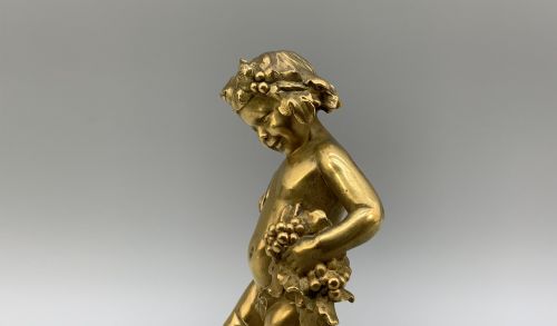 fig 4. A small gilt bronze sculpture depicting an infant Bacchus holding a bunch of grapes, set upon a square green marble plinth.