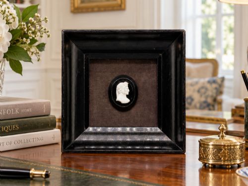 fig 1. A small carved white classical profile portrait cameo mounted on a dark background within a deep black ebonised square frame.