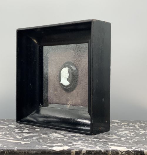 fig 5. A small carved white classical profile portrait cameo mounted on a dark background within a deep black ebonised square frame.