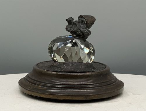 fig 5. A small dark bronze figurine of a bearded dwarf miner holding a hammer overhead, standing on a molded base next to a faceted cut crystal gem.