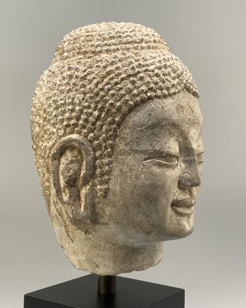 fig 11. A carved limestone Chinese Buddha head featuring downcast eyes, elongated earlobes, and coiled hair, mounted on a black square stand.