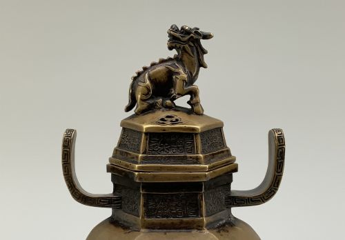 fig 3. A late Qing dynasty hexagonal bronze tripod censer featuring upright side handles, a removable cover topped with a mythical beast finial, and feet shaped as animal masks.