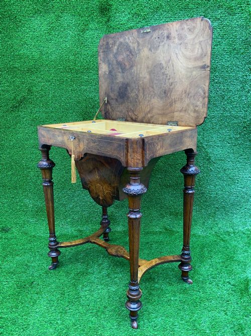 fig 3. A 19th-century burr walnut work table featuring a green leather inset top, floral marquetry inlay, turned legs, and a hanging storage pouch.