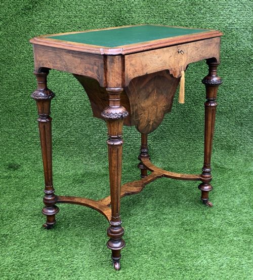 fig 9. A 19th-century burr walnut work table featuring a green leather inset top, floral marquetry inlay, turned legs, and a hanging storage pouch.