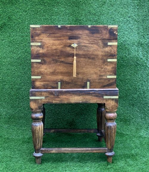 fig 3. A dark teak Anglo-Indian wine cellarette box with brass corner mounts resting on a carved turned-leg wooden stand.