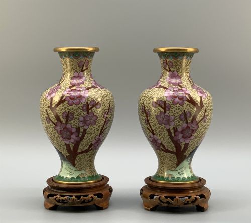 fig 2. A pair of early 20th-century Chinese cloisonne enamel vases featuring pink prunus blossoms and bird motifs on a yellow cloud-scroll ground, resting on carved wooden stands.