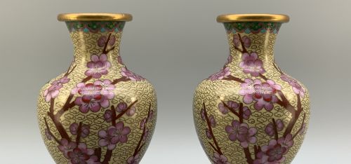 fig 4. A pair of early 20th-century Chinese cloisonne enamel vases featuring pink prunus blossoms and bird motifs on a yellow cloud-scroll ground, resting on carved wooden stands.