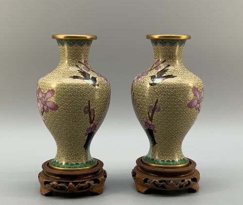 fig 6. A pair of early 20th-century Chinese cloisonne enamel vases featuring pink prunus blossoms and bird motifs on a yellow cloud-scroll ground, resting on carved wooden stands.
