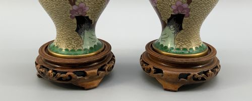 fig 8. A pair of early 20th-century Chinese cloisonne enamel vases featuring pink prunus blossoms and bird motifs on a yellow cloud-scroll ground, resting on carved wooden stands.