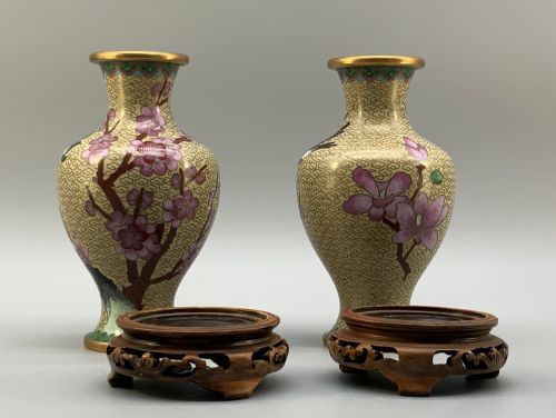 fig 9. A pair of early 20th-century Chinese cloisonne enamel vases featuring pink prunus blossoms and bird motifs on a yellow cloud-scroll ground, resting on carved wooden stands.