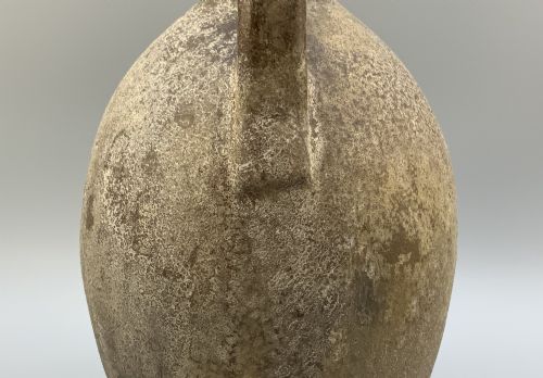 fig 6. A 19th-century salt-glazed stoneware flagon featuring a mottled brown textured surface, narrow neck, flared rim, and a single loop handle.