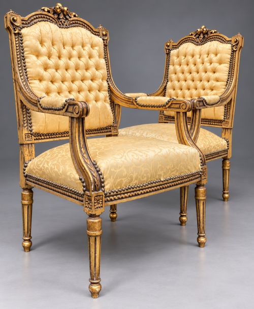 fig 1. A pair of 19th-century giltwood open armchairs featuring carved leaf detailing, button-tufted gold damask upholstery, and fluted front legs.
